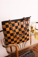 Cartera tipo tote de cuero trenzado a mano con diseño de damero en colores negro y tostado. Cuenta con doble asa de hombro trenzada y cierre superior.