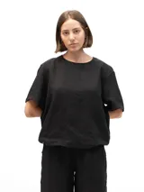 Remera de lino de corte oversize con mangas cortas y cuello redondo. Presenta un diseño minimalista con detalle de botones en la parte posterior.