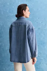 Sobrecamisa de denim de calce amplio y color azul, con cuello clásico, cierre frontal con broches metálicos y bolsillos delanteros con solapa.