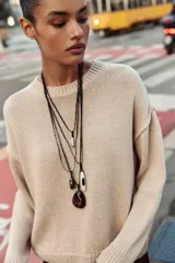 Pack de cuatro collares de cordón de piel negra con diferentes colgantes: uno con pieza metálica en forma de lágrima, otro con piedra marrón, otro con pieza ovalada blanca y negra, y otro con piedra marrón. Todos tienen cierre de lazada y acabados metálicos.