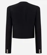 Chaquetilla corta de crepé con cuello redondo y manga larga. Presenta cierre frontal con botones dorados y bolsillos decorativos con solapa en la parte inferior. Diseño estructurado y elegante.