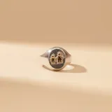 Anillo tipo sello de plata 925 con aplique central de figuras de niños en oro 18k sobre fondo texturizado oscuro.