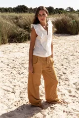 Pantalón de algodón color mostaza, de corte amplio, con cintura elastizada ajustable con lazo. Presenta bolsillos laterales con detalle de flecos.