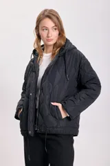 Campera capitoneada negra con diseño acolchado, cierre frontal con botones a presión, capucha con cordón ajustable y cordón en el ruedo.