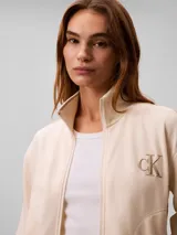 Campera de felpa con cierre de Calvin Klein, color beige, con cuello alto, bolsillos laterales, puños y bajo elásticos, y logo bordado en el pecho.