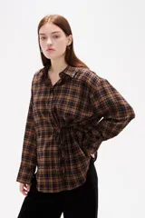Camisa de poliéster con estampado a cuadros, cuello camisero, cierre frontal con botones y detalle de lazo ajustable en la cintura.