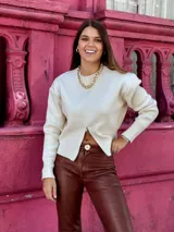 Suéter de punto color crema, con cuello redondo, manga larga y cierre frontal parcial que deja ver parte del abdomen.