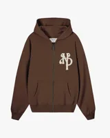 Campera con capucha y cierre frontal de Nude Project, color marrón, con corte boxy y diseño oversized. Presenta un parche bordado en relieve con las iniciales NP en el pecho, capucha amplia y bolsillos tipo canguro.