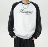 Buzo oversize de corte holgado, color gris melange en el cuerpo con mangas raglán en contraste color negro. Presenta cuello redondo, puños y cintura elastizados, costuras blancas decorativas a lo largo de las mangas y un estampado frontal con la palabra 'Humour' de efecto esfumado.