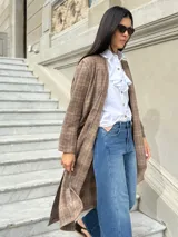 Tapado largo de paño liviano con diseño de cuadros en tonos marrones. Presenta solapas clásicas, bolsillos laterales con detalles en cuero y tajos profundos en los costados.