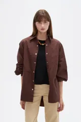 Campera marrón de manga larga confeccionada en algodón, con cuello camisero, cierre frontal con botones a presión y puños elásticos fruncidos.