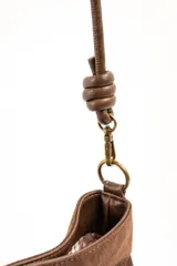 Cartera tipo bandolera de gamuza sintética color marrón, con asa larga decorada con nudos y detalles de herrajes metálicos dorados.