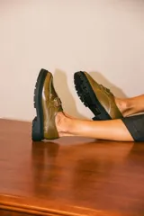 Mocasines de cuero color verde oliva con suela track negra de plataforma. Presentan una tira decorativa sobre el empeine con hebilla metálica dorada ajustable en el lateral.