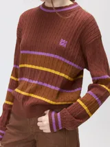 Sweater clásico de punto cable con cuello redondo a la base, mangas largas y fit al cuerpo. De color marrón con franjas horizontales violetas y amarillas, cuenta con el cuello, puños y ruedo acanalados, además de un pequeño logo bordado en el pecho.