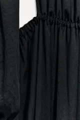 Vestido midi negro de cuello redondo y manga larga abullonada con puños elásticos. Presenta cintura elastizada y espalda descubierta con cierre de botón en el cuello.