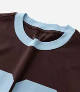 Remera de algodón color marrón con cuello redondo y bordes de las mangas en color celeste. Presenta una estampa frontal con el número 86 en color celeste.