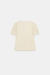 Camisa de gasa color crudo con escote en pico, manga corta abullonada con terminación en volante y cierre frontal con botones ocultos y lazada. Presenta delicados detalles de bordados a tono en toda la prenda.