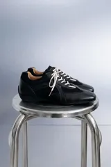 Zapatillas negras de estilo urbano con cordones blancos, confeccionadas en cuero sintético y poliéster, con diseño de paneles y suela plana.