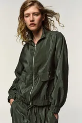 Chaqueta bomber negra de cuello subido y manga larga. Tiene bolsillos delanteros con solapa y cierre de botón a presión, acabados elásticos en puños y bajo, y cierre frontal con cremallera.