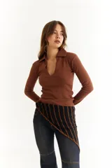 Top de manga larga color verde petróleo, con cuello polo y escote en V pronunciado. Presenta recortes diagonales en el frente y un pequeño bordado en el puño.