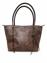 Cartera tipo tote bag de cuero vacuno marrón, con detalles de trenzado artesanal en los laterales y flecos colgantes decorativos. Cuenta con doble asa de hombro y cierre superior.