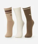 Kit de tres pares de medias deportivas Puma de caña larga. Un par es beige con dos rayas marrones y logo de Puma. Otro par es blanco liso. El tercer par es marrón oscuro con dos rayas blancas y logo de Puma. Todas están confeccionadas en algodón.