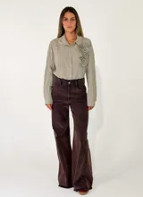 Camisa de corte oversize color beige, con cuello clásico, cierre frontal de botones y detalle de flores de tela aplicadas en el pecho.