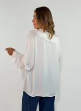 Blusa de satén color blanco con escote en V, cuello con volados y mangas largas con puños también decorados con volados.