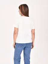 Remera lila de corte recto y mangas cortas, con estampado pequeño de un gato blanco con gorro rojo, gafas de sol y copa de vino, junto a la frase 'J'adore'.