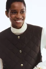 Chaleco guateado color marrón oscuro, con cuello redondo, cierre frontal con botones a presión dorados y dos bolsillos de parche en la parte delantera.