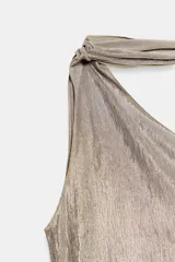 Top asimétrico de tejido con efecto metalizado color plateado, con escote de un solo hombro y detalle de foulard integrado en el cuello. Presenta un diseño sin mangas y dobladillo inferior asimétrico.