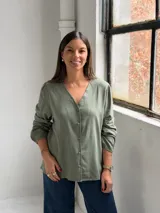 Blusa de color verde oliva con escote en V, cierre frontal con botones y mangas largas con puños elásticos.