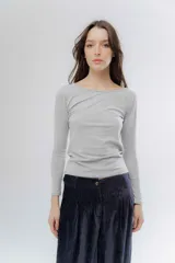 Remera básica de manga larga en color gris melange, confeccionada en algodón suave. Presenta un diseño de cuello redondo y un detalle de etiqueta decorativa en el puño.