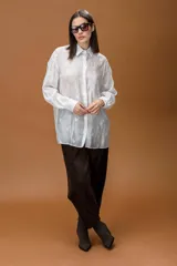 Camisa blanca de corte holgado y tejido semitransparente, con delicados bordados de mariposas en toda la prenda. Presenta cuello clásico, cierre frontal con botones y mangas largas con puños abotonados.