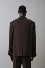 Blazer de corte relaxed fit color marrón, confeccionada en tejido con mezcla de lana. Presenta cuello con solapas de muesca, manga larga, bolsillos de vivo en la cadera y cierre frontal de botonadura con dos botones. Cuenta con forro interior combinado a contraste y abertura en el centro de la espalda.