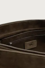 Bandolera de piel con acabado en serraje, color marrón, con compartimento principal con cierre de solapa y cremallera, bolsillos interiores y asa de hombro ajustable.