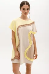 Vestido corto de algodón, con bloques de color en tonos pastel (amarillo claro, beige y rosado pálido) unidos por volados fruncidos en tonos marrón claro y amarillo. Presenta cuello redondo y mangas cortas.