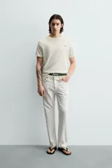 Camiseta de corte relajado, color crudo, con cuello redondo y manga corta. Presenta un pequeño estampado gráfico en el pecho con la inscripción 'Whitsunday Island'.