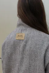 Campera de paño de lana en color beige jaspeado, con diseño oversize. Presenta detalles en pana color marrón chocolate en los puños y en las tapas de los bolsillos frontales. Cuenta con cierre frontal de botones grandes y cuello alto.
