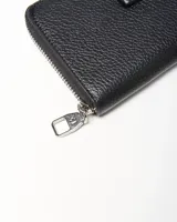 Billetera fichero de cuero sintético negro con cierre perimetral y aplique frontal con el logo de la marca en placa metálica plateada.