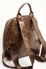 Mochila de cuero sintético marrón con efecto craquelado, asa superior y placa metálica frontal con el logo de la marca.