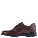 Zapato de vestir para hombre color marrón chocolate, confeccionado en cuero con textura granulada. Presenta costuras decorativas en contraste, cierre con cordones y suela de goma negra con tecnología de amortiguación.
