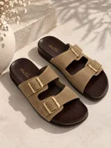 Sandalia plana tipo Birkenstock modelo Lena, con dos tiras anchas en color beige, hebillas metálicas doradas y plantilla de madera oscura.