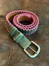 Cinturón de cuero verde con detalle de costura entrelazada en color fucsia a lo largo de los bordes. Cuenta con hebilla metálica y remaches en color plateado.