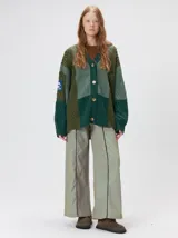 Cardigan oversize de tejido de punto grueso con diseño de bloques de color en tonos tierra. Presenta cuello en V, cierre frontal con botones, mangas largas con terminación abullonada y parches decorativos en el pecho y hombro.