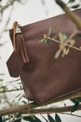 Neceser de cuero marrón con cierre superior y tirador de cuero con flecos.