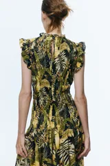 Vestido midi de mezcla de viscosa, con cuerpo fruncido, cuello de volados y sin mangas con volados en los hombros. Presenta costura fruncida en la cadera y falda amplia con vuelo. Estampado de hojas y flores tropicales en tonos verdes, amarillos y negros.