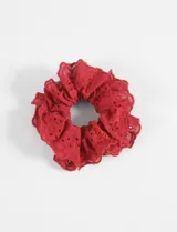 Gomita para el pelo tipo scrunchie confeccionada en tela broderie de color rojo, con diseño fruncido y bordes con detalle calado.