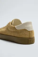 Zapatilla de cordones confeccionada en piel con acabado de serraje. Presenta un diseño liso con detalle en color a contraste en la pieza del talón y suela plana de goma a contraste.