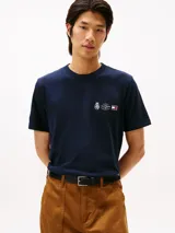 Remera de cuello redondo en color azul marino, confeccionada en algodón regenerativo. Presenta un pequeño logo bordado en el pecho con diseño de escudo y la bandera distintiva de la marca.